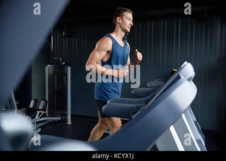 In voller Länge Porträt der muskulöse Sportler Hören von Musik über Kopfhörer und mit Laufband, während sie in der Ausbildung an modernen Fitnessraum gewickelt, Profil vi. Stockfoto