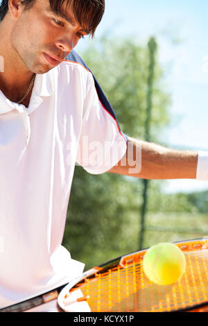 Junge Tennisspieler, der die Kugel mit dem Schläger Stockfoto