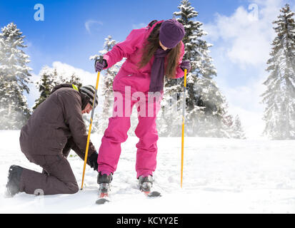 Jungen Menschen hilft, ihre Freundin ihr Ski Winter Hintergrund zu setzen Stockfoto