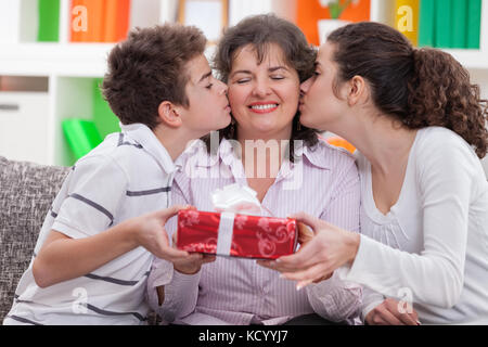 Glückliche Mutter, die Küsse von ihren Kindern empfängt und lächelt. Stockfoto