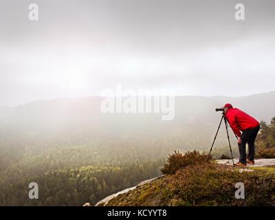 Photographr in den Sucher der DSLR-Kamera auf Stativ. Künstler fotografieren Berg und trübe Landschaft. Man prüfen Bild auf Stockfoto