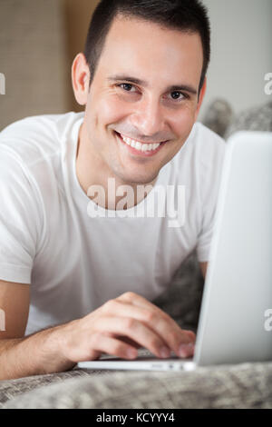 Fröhlicher Mann auf dem Sofa mit Laptop Stockfoto