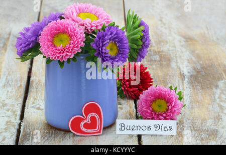 Buenos dias (Guten Morgen in Spanisch) mit bunten daisy Blumenstrauß in blauer Vase auf Holzmöbeln im Landhausstil Oberfläche Stockfoto