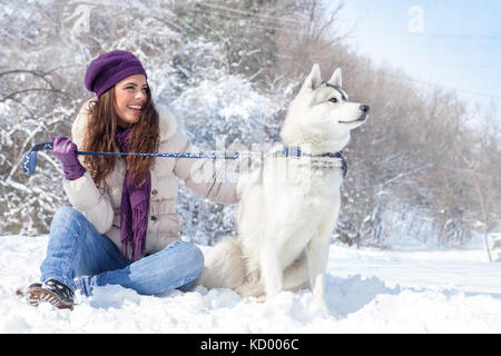 Junge schöne Frau sitzt mit Husky Hund im Winter Forest Stockfoto