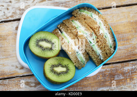 Braunes Brot Sandwiches mit Frischkäse und Gurken und Kiwi in blau Lunch Box Stockfoto
