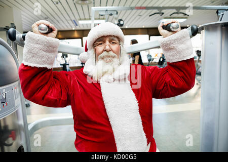 Santa claus macht Übung auf der Maschine im Fitnessstudio Stockfoto