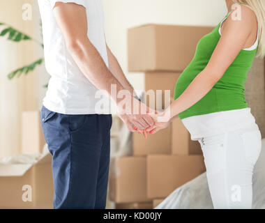 Süße schwangere Frau halten sich an den Händen und ihren Mann stehen vor Boxen während der Bewegung im neuen Haus Stockfoto