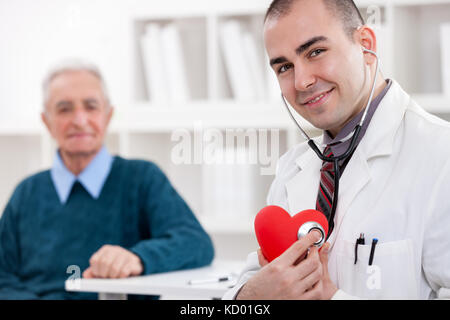 Arzt halten roten Herzen Symbol mit Patienten im Hintergrund Stockfoto