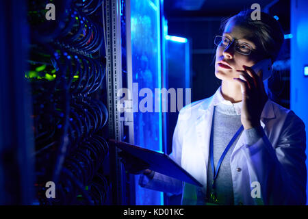Portrait von schönen weiblichen Wissenschaftler arbeiten mit supercomputer im Neonlicht, spricht von Telefon und halten digitale Tablet Stockfoto