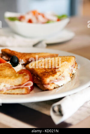 Eine Platte mit einem köstlichen Schinken Panini mit Tomate, Mozzarella, Oliven und Mayonnaise, serviert mit einem Beilagensalat Stockfoto