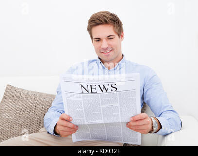 Glücklicher junger Mann sitzt auf der Couch lesen Zeitung Stockfoto