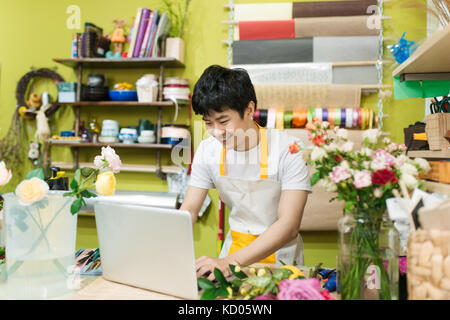 Gerne asiatische männlichen Florist mit Laptop am Zähler in Flower Shop Stockfoto