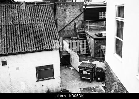 Schwarze und weiße monochrome Bild eines städtischen Gasse mit wheely Bins verfallen und Backsteinbauten mit keine Personen Stockfoto