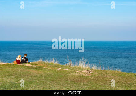 Junges Paar sitzen auf der Spitze einer Klippe Flanke an Berry Head, Brixham, Devon am klaren, blauen Horizont, an einem sonnigen Sommer. Stockfoto