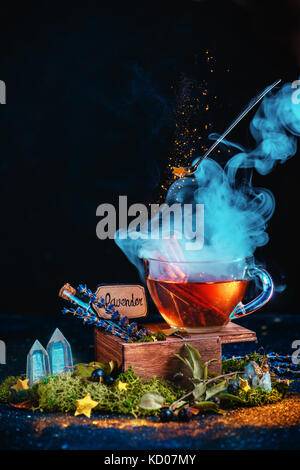 Magische noch Leben mit einer Tasse Tee, Dampf, fliegende Oldtimer Löffel, Stardust, Röhrchen mit Zaubertrank Zutaten, Kristalle und Moos. Hexe Workplace Konzept. Stockfoto