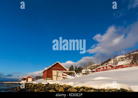 Typisch norwegische warmes und gemütliches Haus am See an einem Fjord in Troms County, Norwegen. Die Sonne steht tief über dem Horizont und der Himmel ist Stockfoto