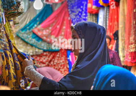 Provinz Fars, Shiraz, Iran - 19 April 2017: Eine junge Iranerin im hijab tragen den Stoff für den Kauf in einem Textilgeschäft in der Basar wählen Stockfoto