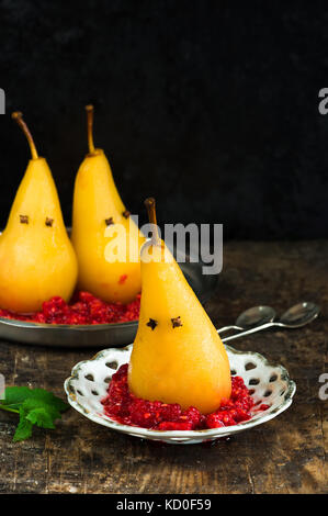 Birne pochiert in süßen Sirup auf zerquetschte Himbeeren, dargestellt als Geister. Halloween Essen Idee. Stockfoto