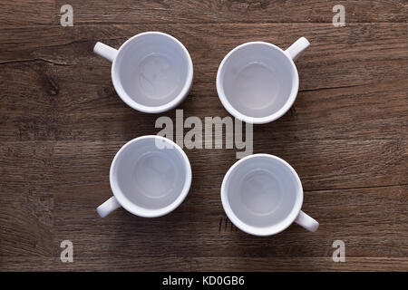 Essen Konzept - Blick von oben auf die vier weißen Becher ohne Untersetzer auf grau braun Holz Tisch. Leere Keramik Becher Stockfoto