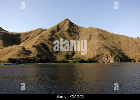 Kleines Boot vor der Küste von Bergen mit grüner Vegetation im blauen Ozean Wasser in Labuan Bajo, Flores, Indonesien. Stockfoto