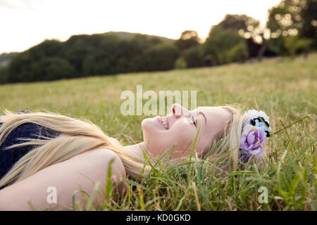 Frau mit Blumen im Haar auf Gras liegend lächelnd Stockfoto