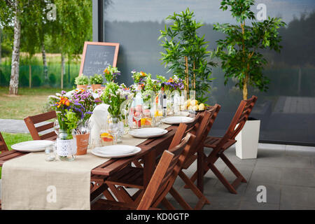 Tisch zubereitet mit Blumenarrangements und Platten für das Mittagessen auf der Terrasse Stockfoto