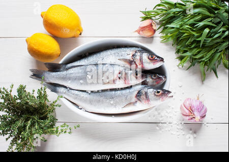 Rohe frische Fisch auf dem Holztisch in die weiße, ovale Platte, Grüns, Zitronen und Salz Stockfoto