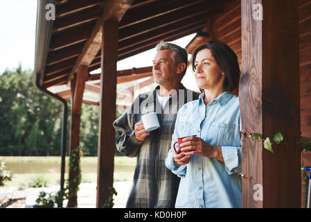 Reifes Paar stehend auf Kabine Veranda, Holding tin Cups, Anzeigen suchen Stockfoto