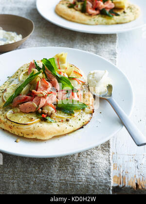 Mini Pizza, gekrönt mit geräucherter Forelle und Artischocke, auf weiße Platte Stockfoto