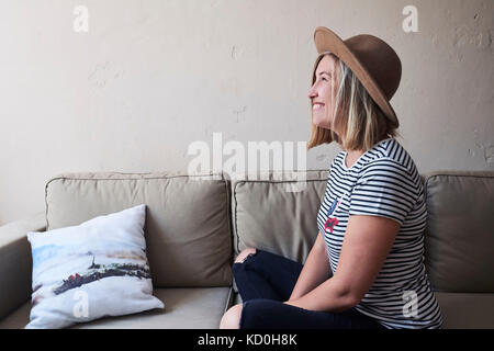 Frau sitzt auf einem Sofa, lächelnd, Seitenansicht Stockfoto