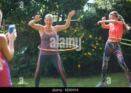 Mädchen Fotografieren von Mutter und Schwester im Teenageralter hoola hooping in Garten Stockfoto