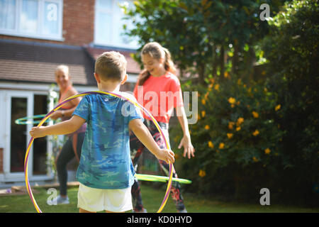 Junge, Mutter und Schwester im Teenageralter hoola hooping in Garten Stockfoto