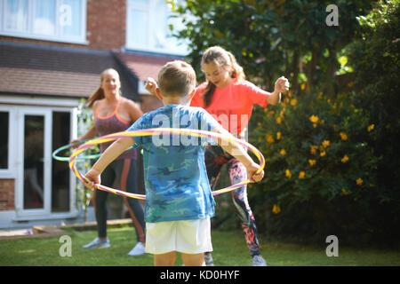 Reife Frau mit Sohn und Tochter im Teenageralter hooping hula im Garten Stockfoto
