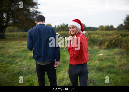 Ansicht der Rückseite des jungen Paares im Santa Hut und Weihnachten Lichterkette bummeln in Feld Stockfoto