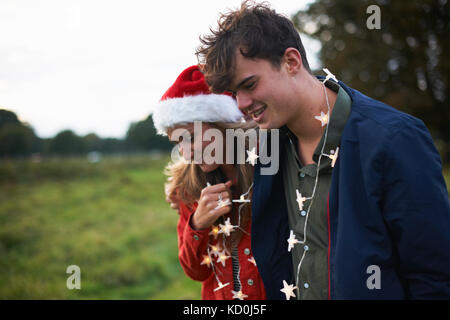 Junges Paar in Santa Hut und Weihnachten Lichterkette bummeln in Feld Stockfoto