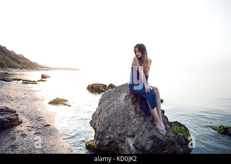 Junge Frau sitzt am Strand Felsen, Odessa, Ukraine Stockfoto