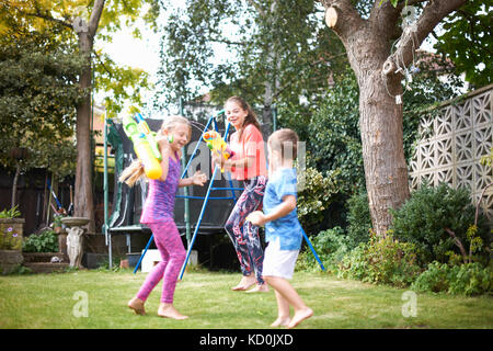 Junge und seine Schwestern in Wasser Gun zu kämpfen, im Garten Stockfoto