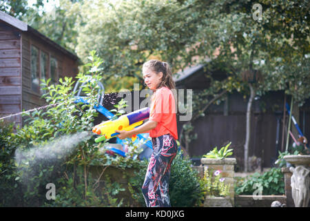 Junges Mädchen squirting Wasserpistole im Garten Stockfoto