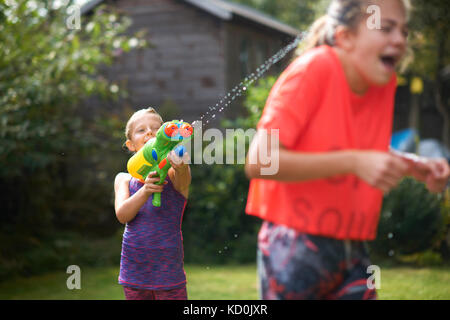Junge sein halbwüchsiger Schwestern Bespritzen mit Wasser Gewehr im Garten Stockfoto