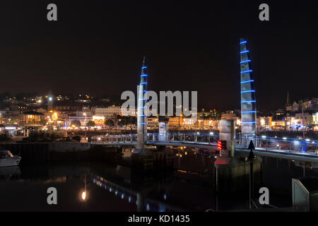 Beleuchtete Nachtaufnahme des inneren Hafens von Torquay mit der Millenium Bridge im Vordergrund und beleuchteten Hafengeschäften und Restaurants. Stockfoto
