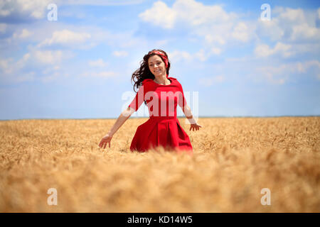 Schöne Mädchen im roten Kleid zu Fuß durch ein Weizenfeld. Stockfoto