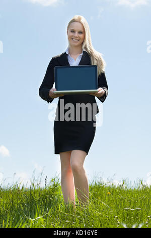 Glückliche Junge Geschäftsfrau, Die Vor Ort Einen Laptop Vorstellt Stockfoto