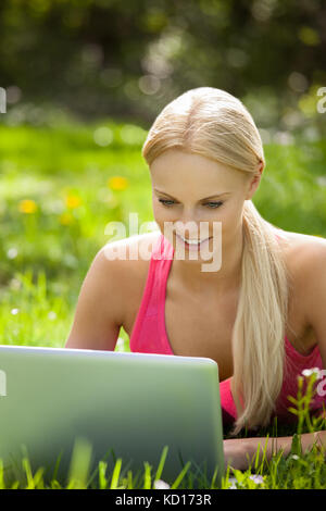 Glücklich schöne Frau liegend auf dem Rasen mit Laptop Stockfoto