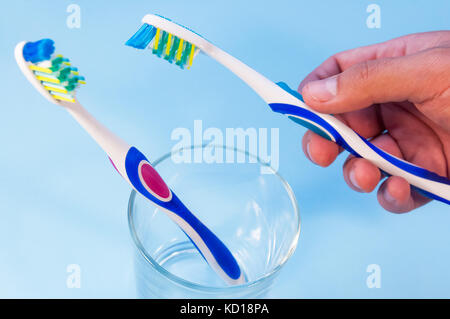 Zwei Zahnbürsten in einem Glas. die Hand eines Mannes dauert eine Zahnbürste. Stockfoto