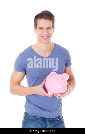 Porträt eines glücklichen jungen Mannes hält Sparschwein Over White Background Stockfoto