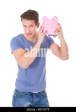 Porträt eines glücklichen jungen Mannes hält Sparschwein Over White Background Stockfoto