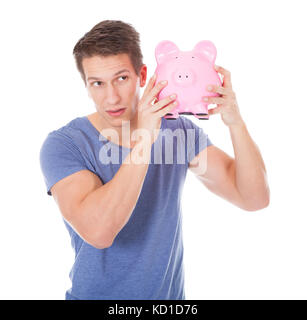 Porträt eines glücklichen jungen Mannes hält Sparschwein Over White Background Stockfoto