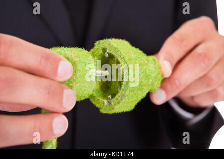 Nahaufnahme der Geschäftsmann hand mit Gras bedeckt elektrischen Stecker und Buchse Stockfoto