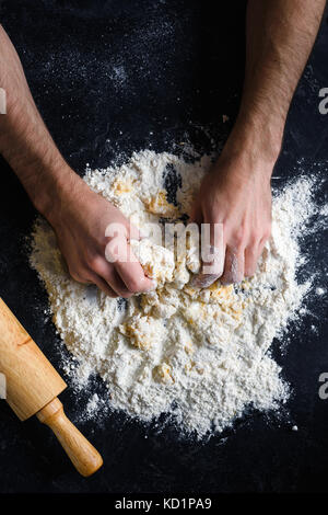 Koch und Pastateig. Mann Hände kneten den Teig auf dunklem Hintergrund, Ansicht von oben. Bäckerei, Konditorei Vorbereitungen Konzept Stockfoto