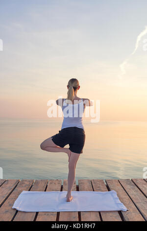 Ansicht der Rückseite des junge Frau saß auf dem Handtuch Üben Yoga von Meer bei Sonnenuntergang Stockfoto